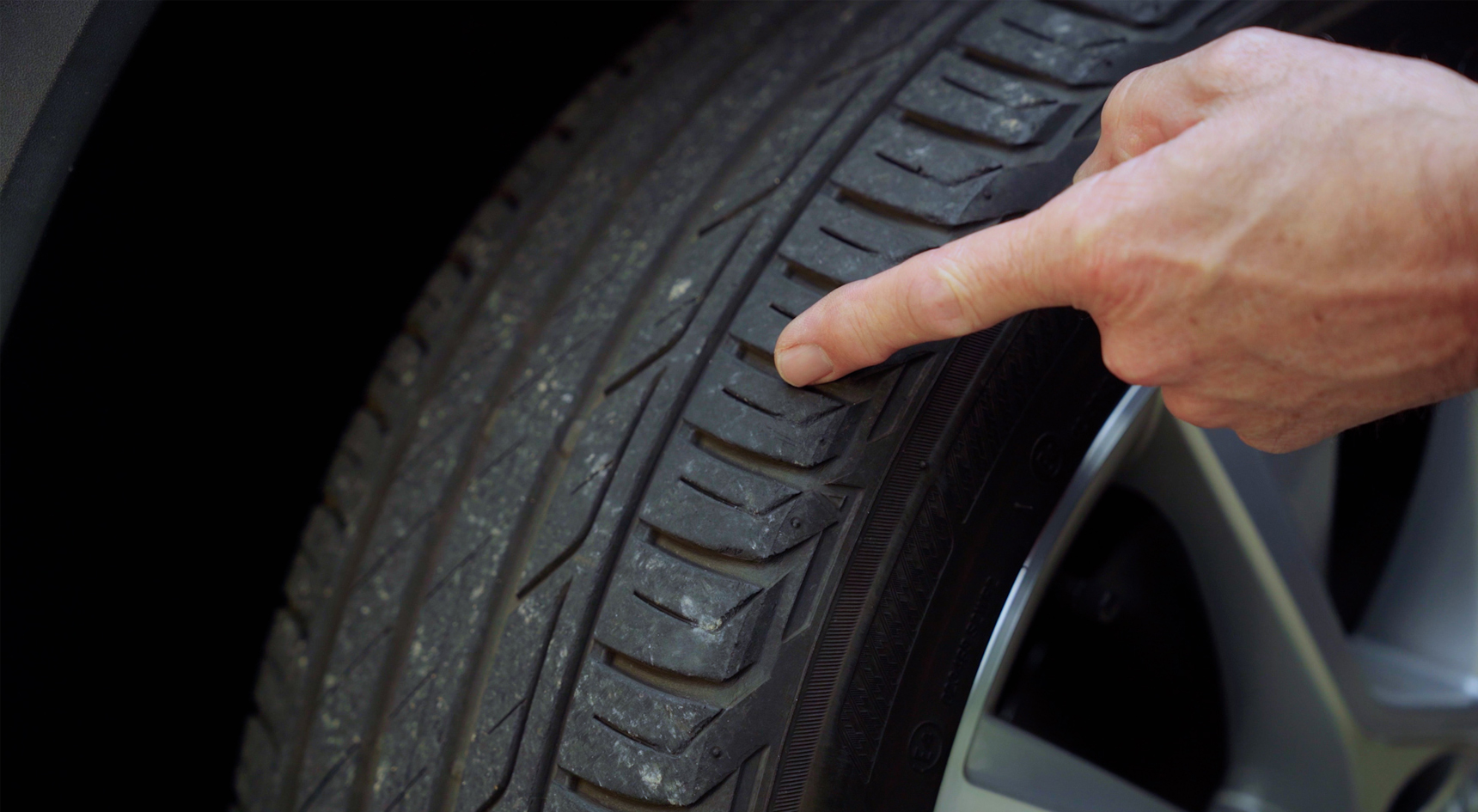 A person pointing at the tread on a tyre to show how the minimum depth.