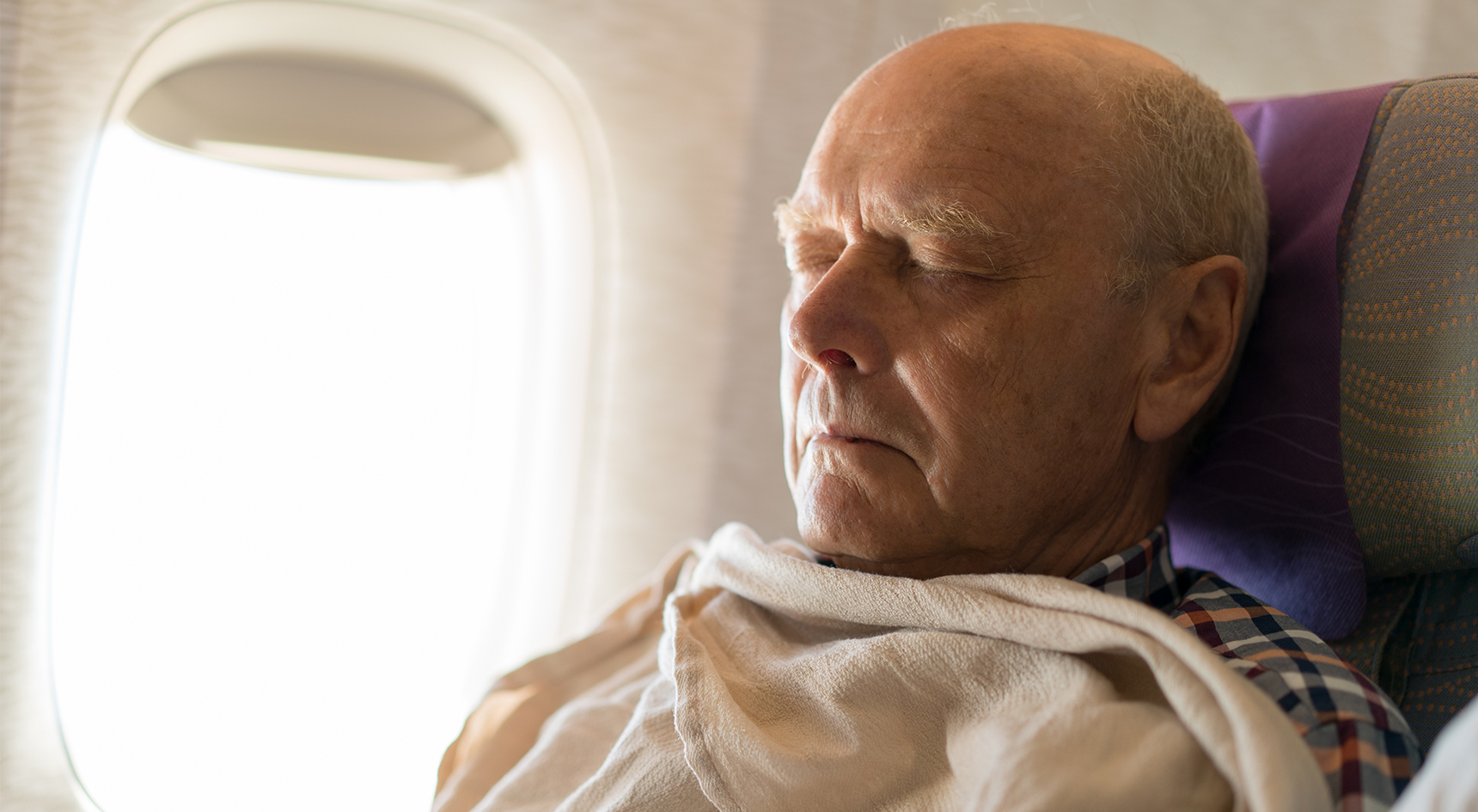 Man asleep on a plane covered in a blanket