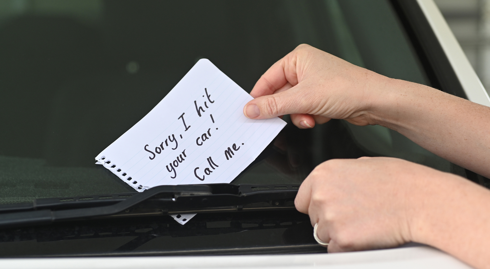 A person placing a note under a windscreen wiper.
