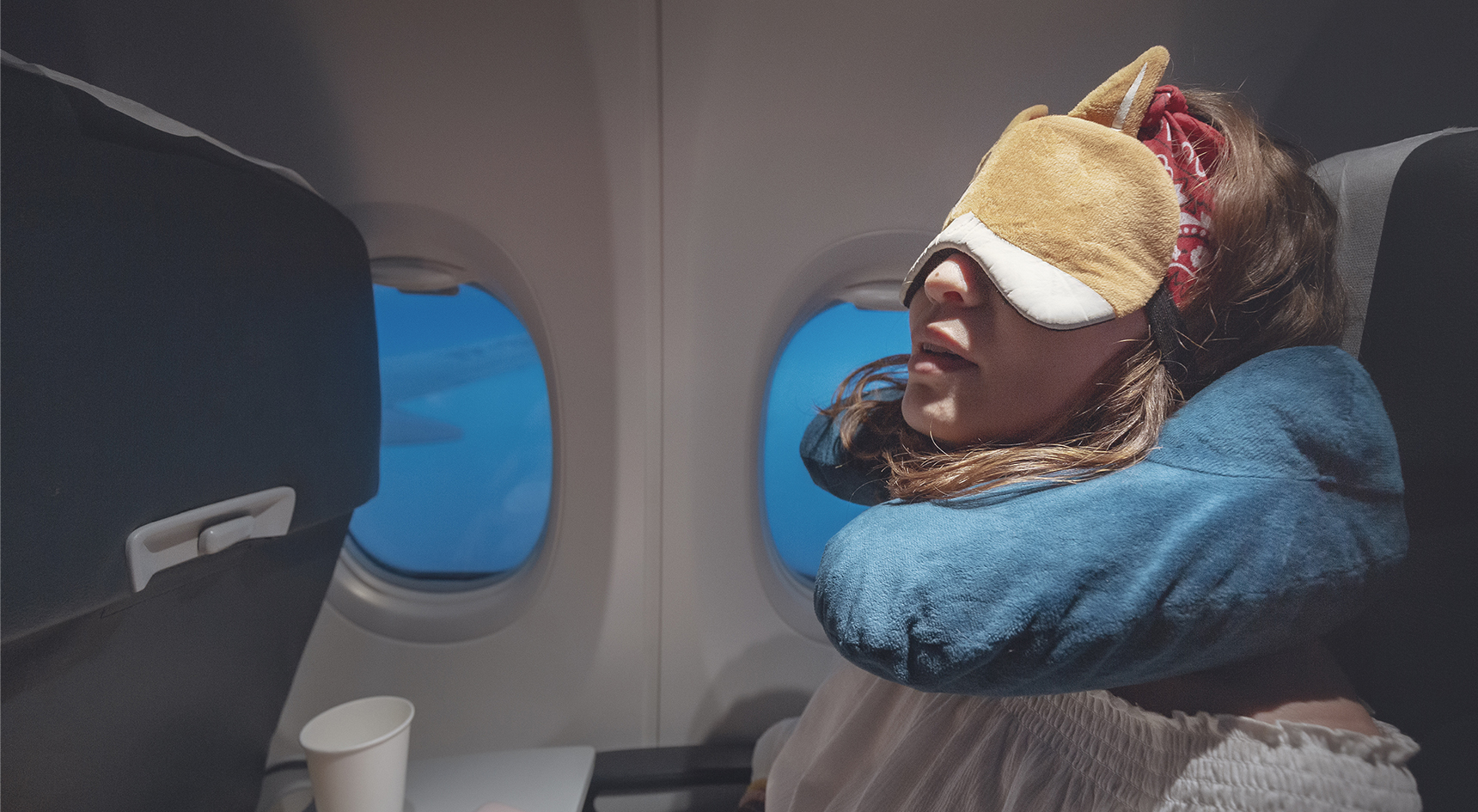 Woman sleeping on a plane with eye mask and neck pillow
