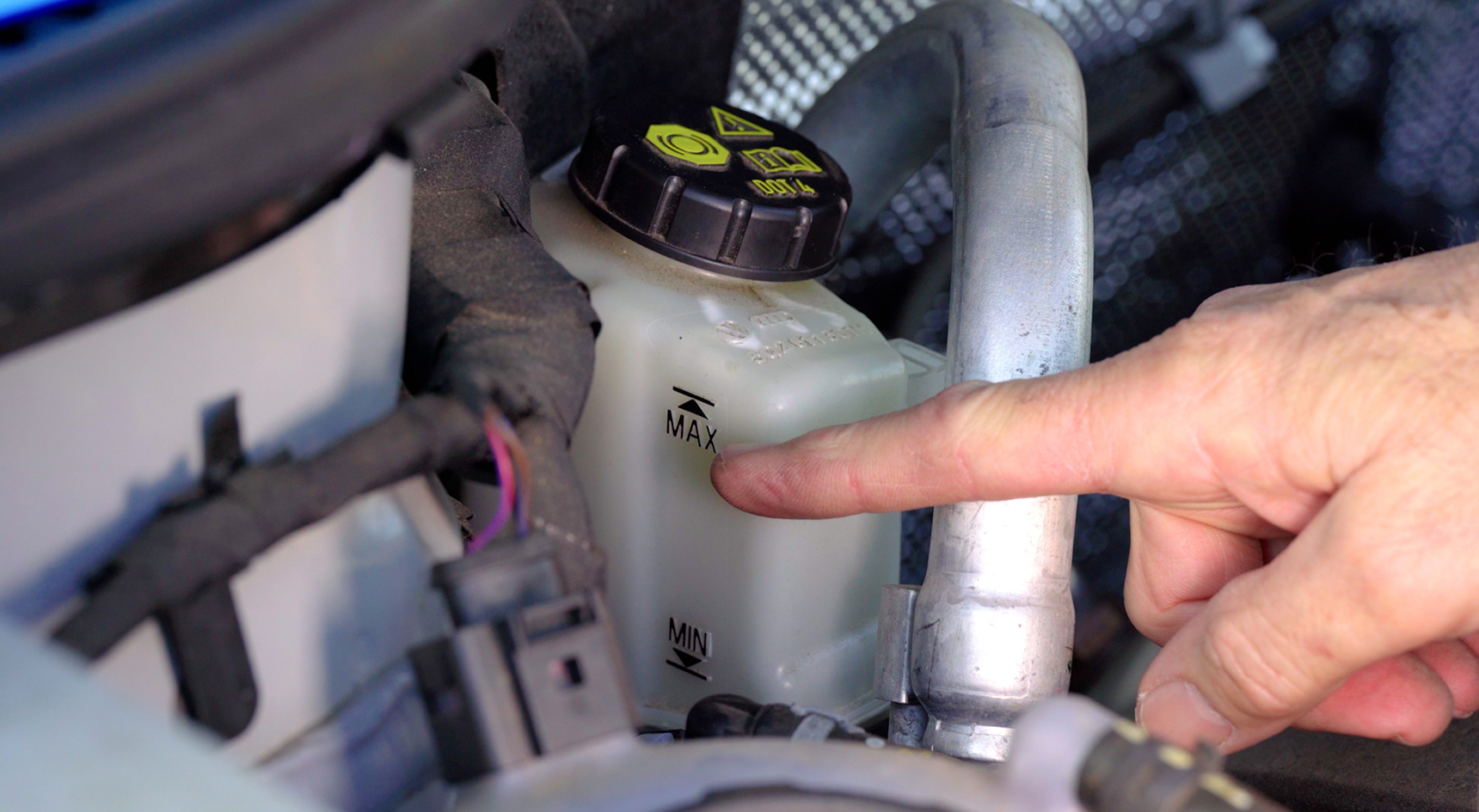 Man pointing to the maximum and minimum lines on brake fluid reservoir