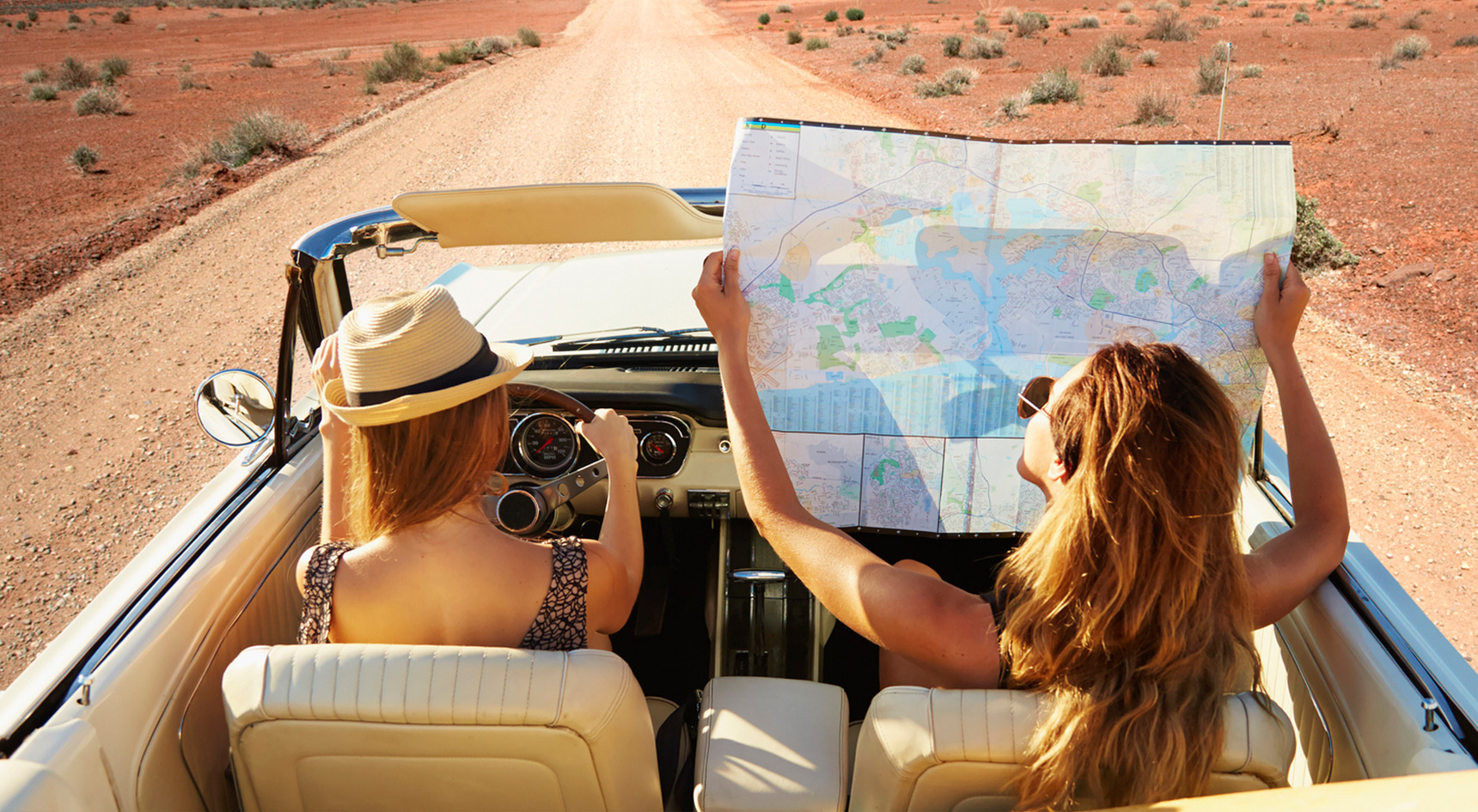Two women driving on an open road, one holding a map