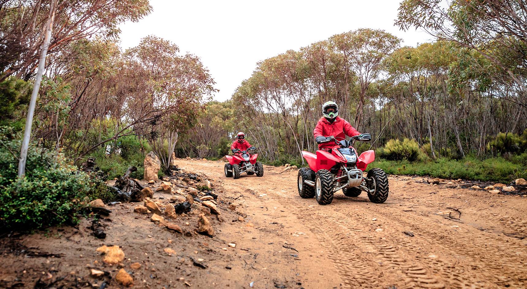 Two people on quad bikes on a dirt road