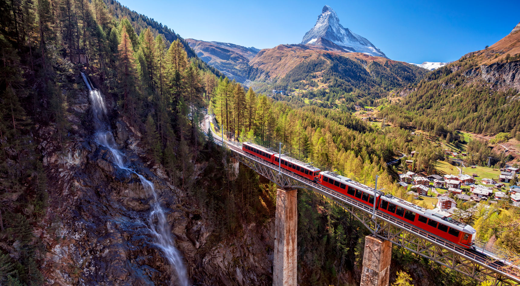 Bright red train on a viaduct next to a waterfall