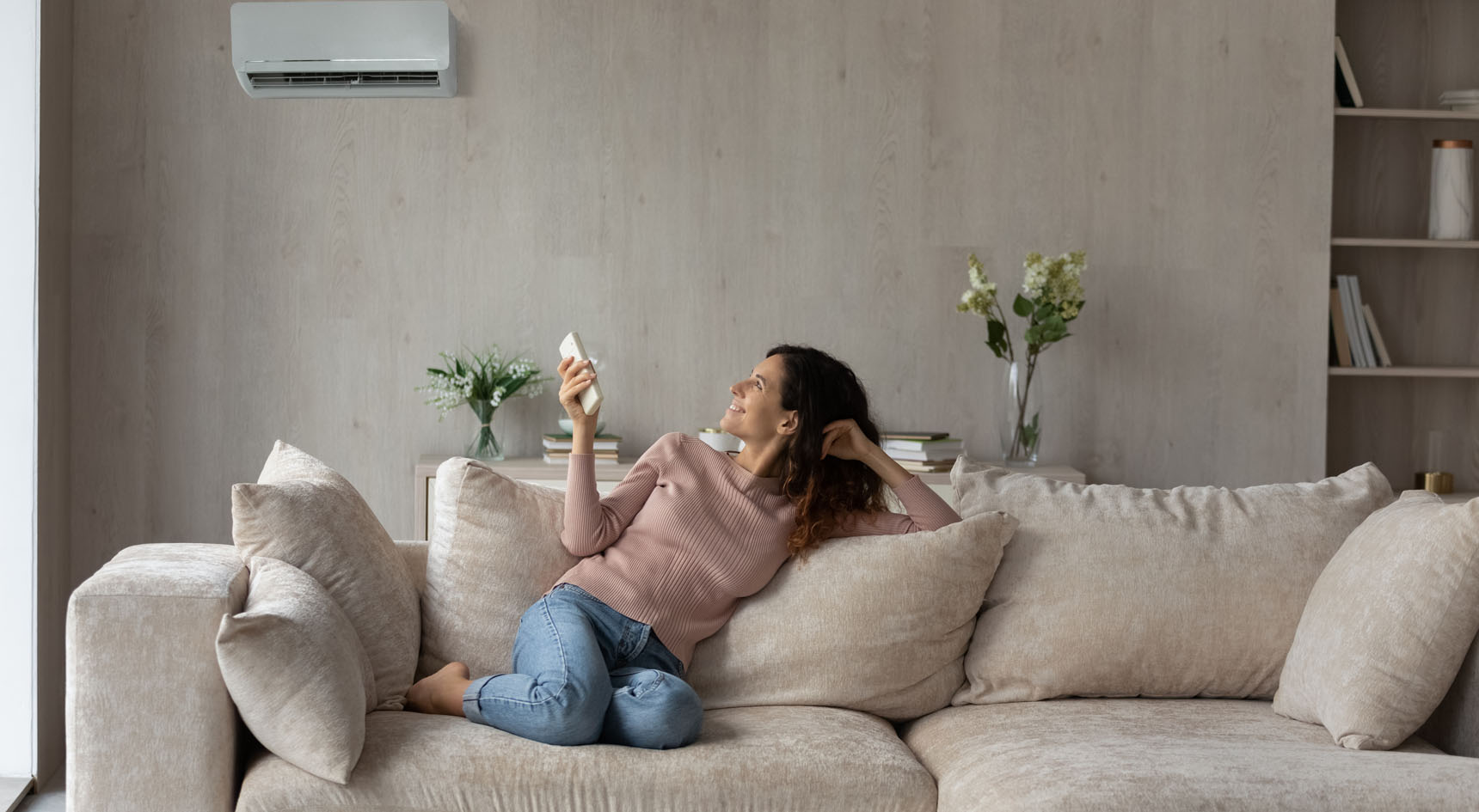 A lady sitting on a couch turning on her air-conditioning