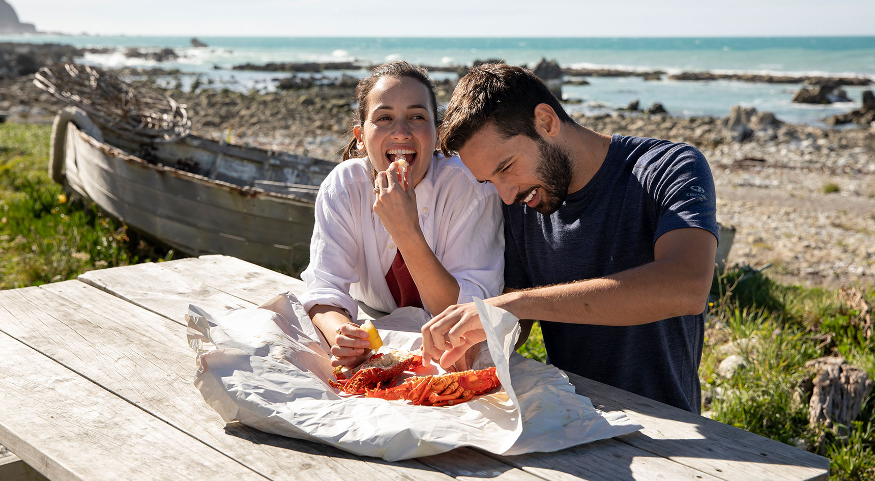 Two people enjoying fish and chips by the beach in New Zealand