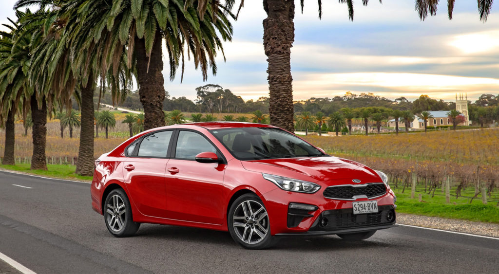 Red Kia Cerato on the road with vines in the background.