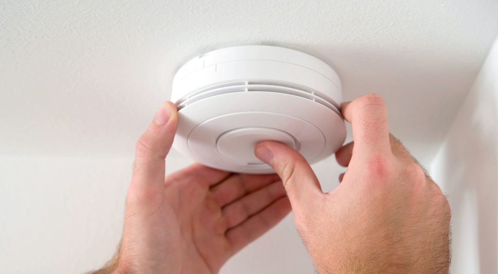 Person's hands on smoke alarm as they check it is in working order.