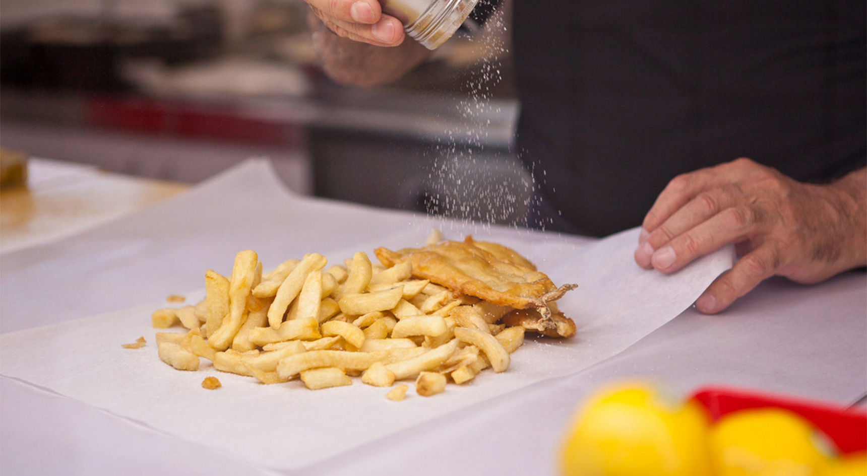 a man seasoning fish and chips on grease proof paper.