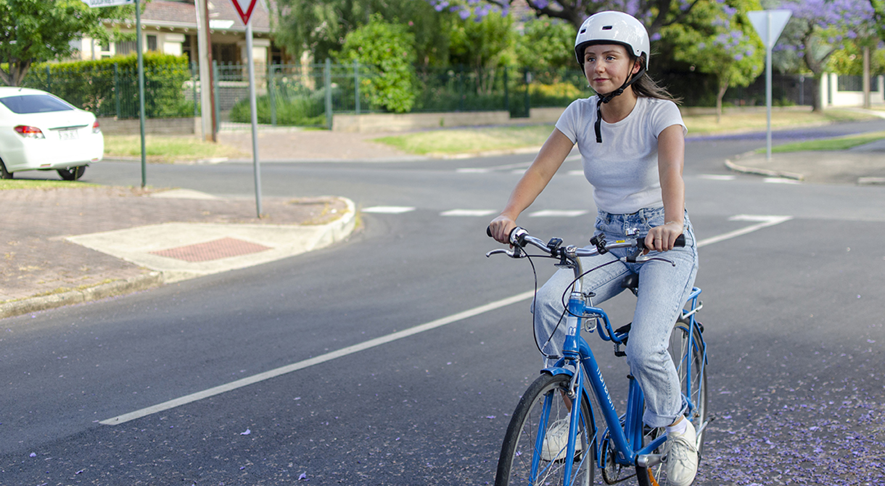 A lady riding down the road on her bike wearing a helmet.