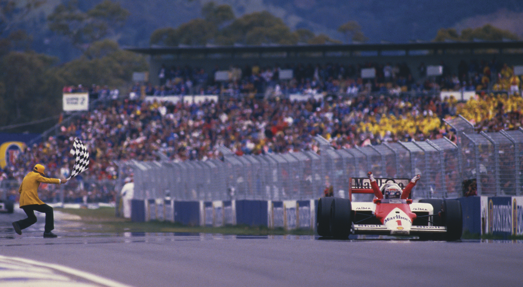 Historic image of Glen Dix exuberantly waving Alain Prost across the finish line at the 1984 Australian Grand Prix.