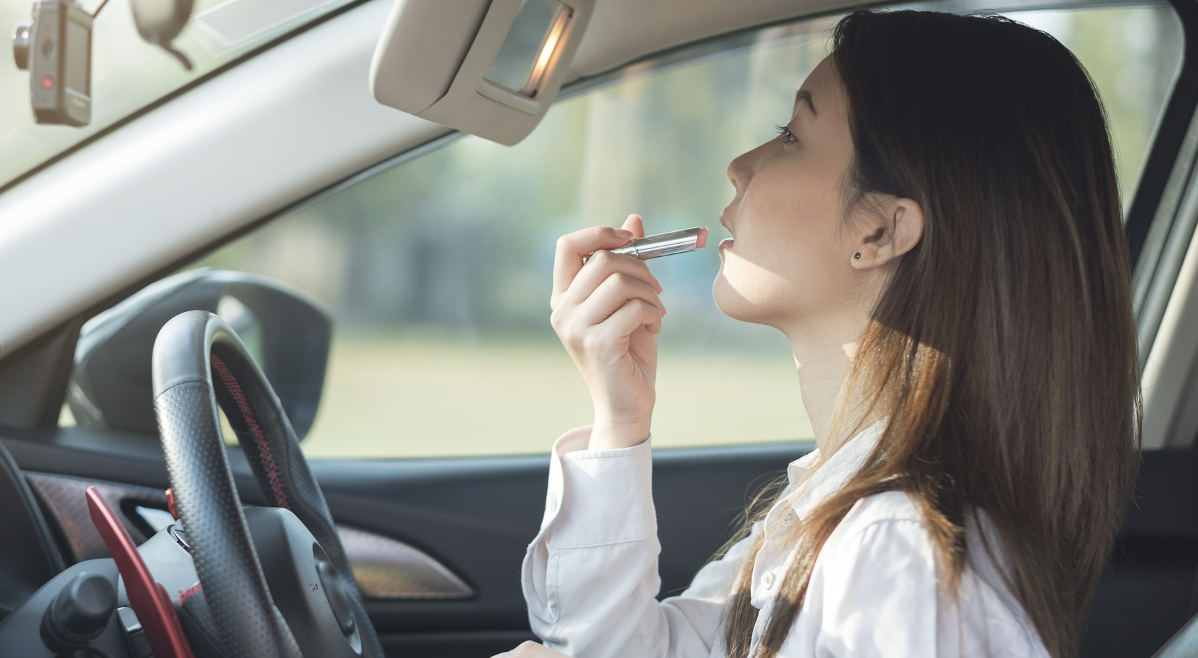 lady applying lipstick while behind the wheel.