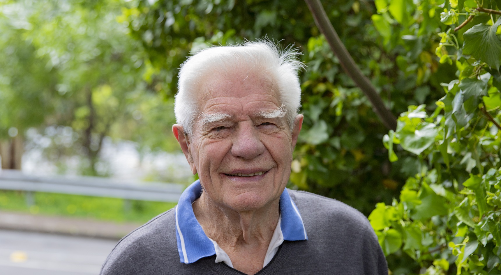 Jim smiles as he looks directly into the camera, with green trees in the background.