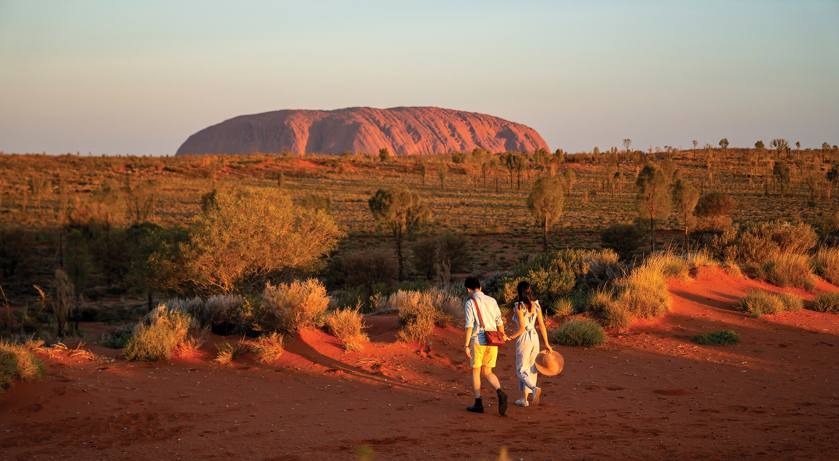 Couple walking with Uluru, NT in the backyground
