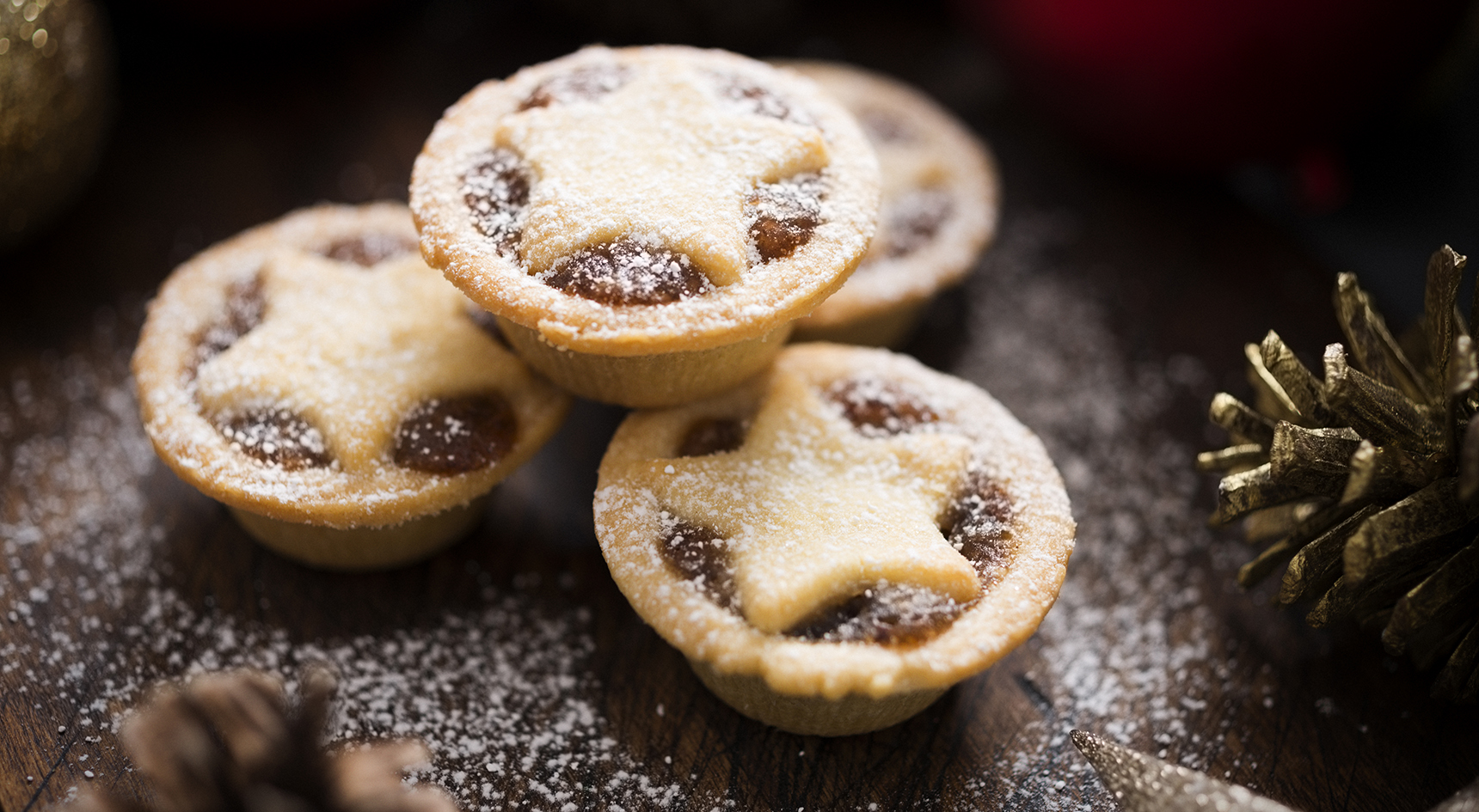 Three small mince pies, dusted with icing sugar with Christmas decorations.
