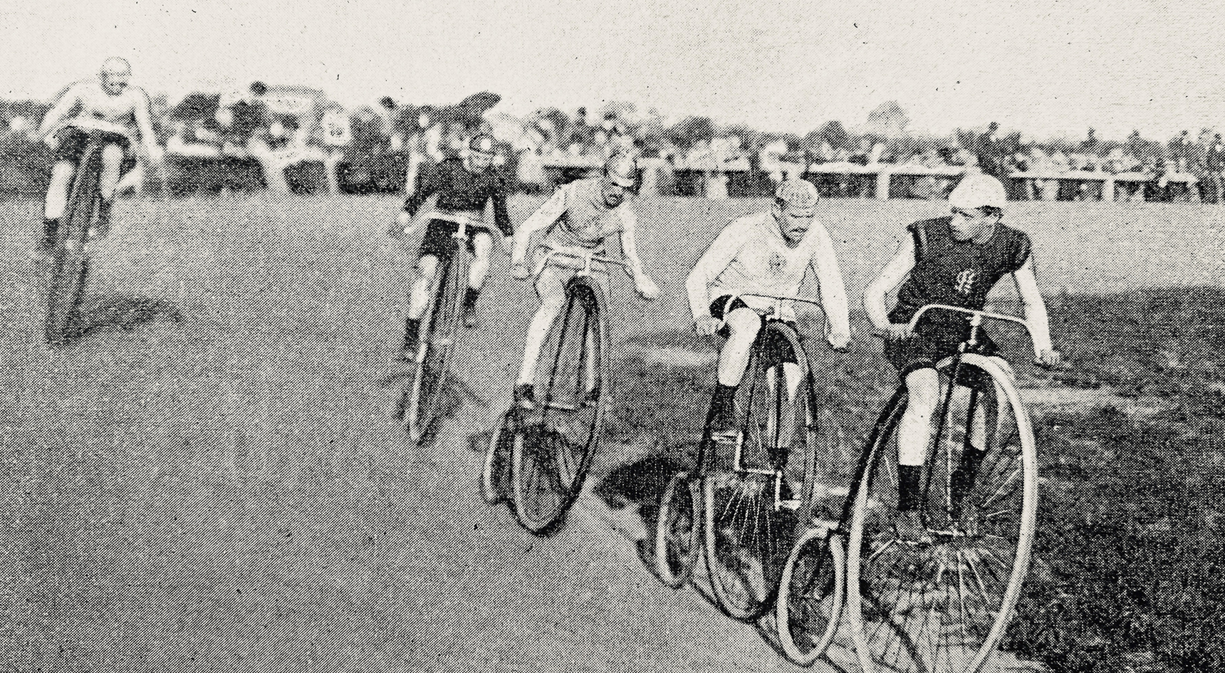 A black and white photo of people racing on penny farthings. 