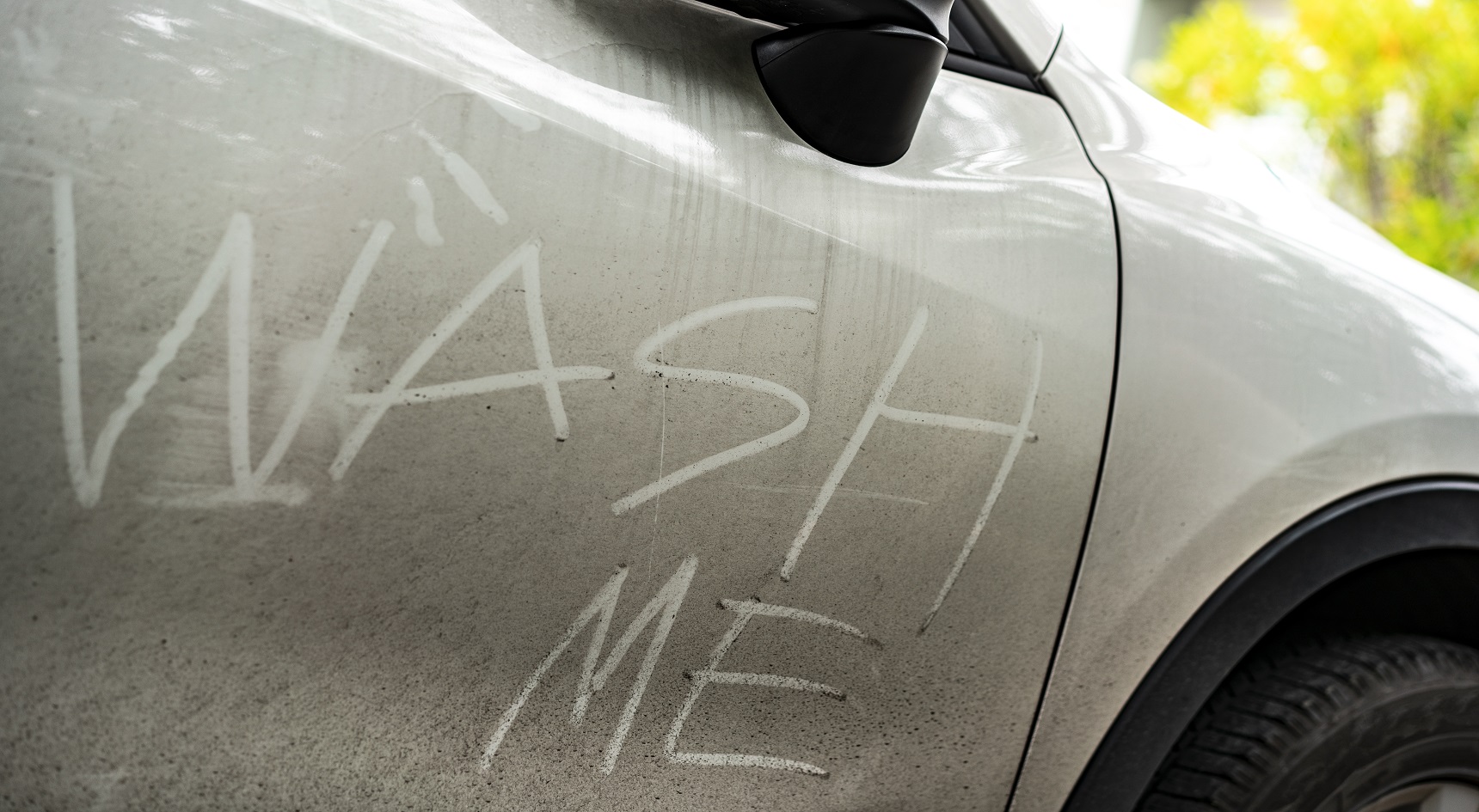 Dirty white car with the words 'Wash me' written in dust.