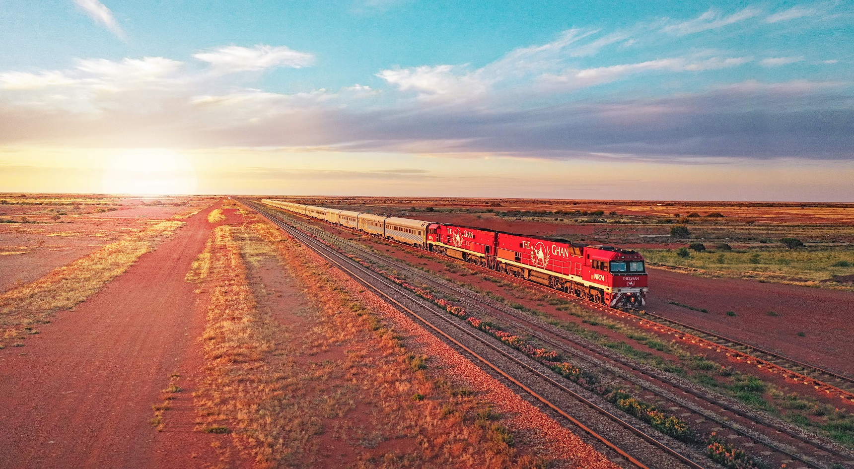 The Ghan travelling in the outback with the sun in the distance.