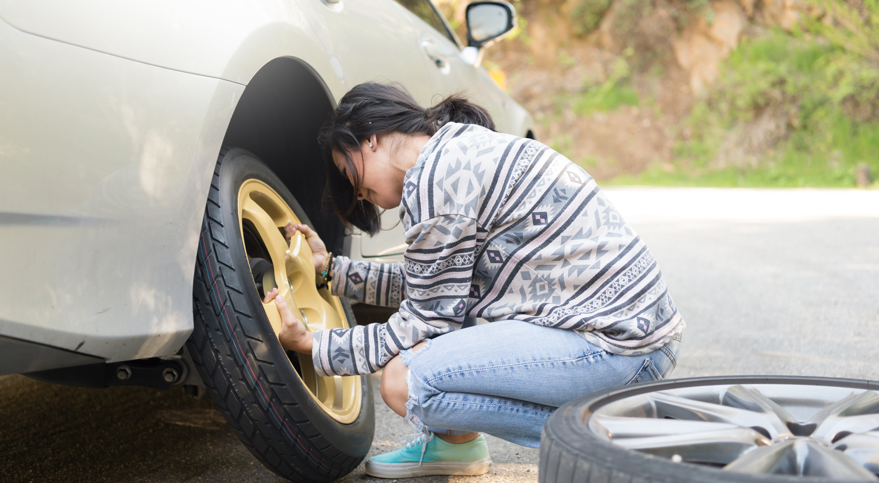 A woman changing her tyre on the side of the road