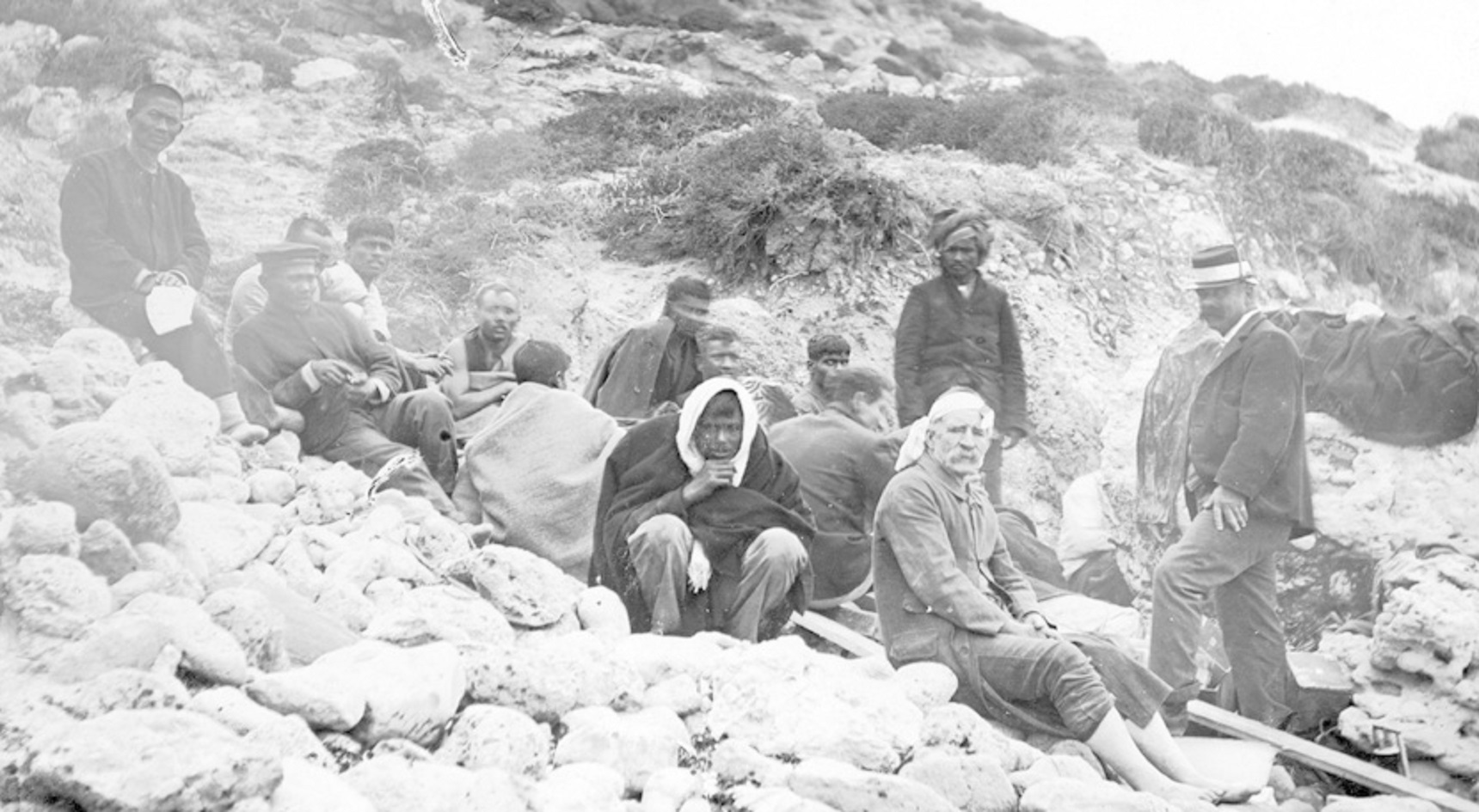 An old image of shipwreck survivors sitting on rocks.