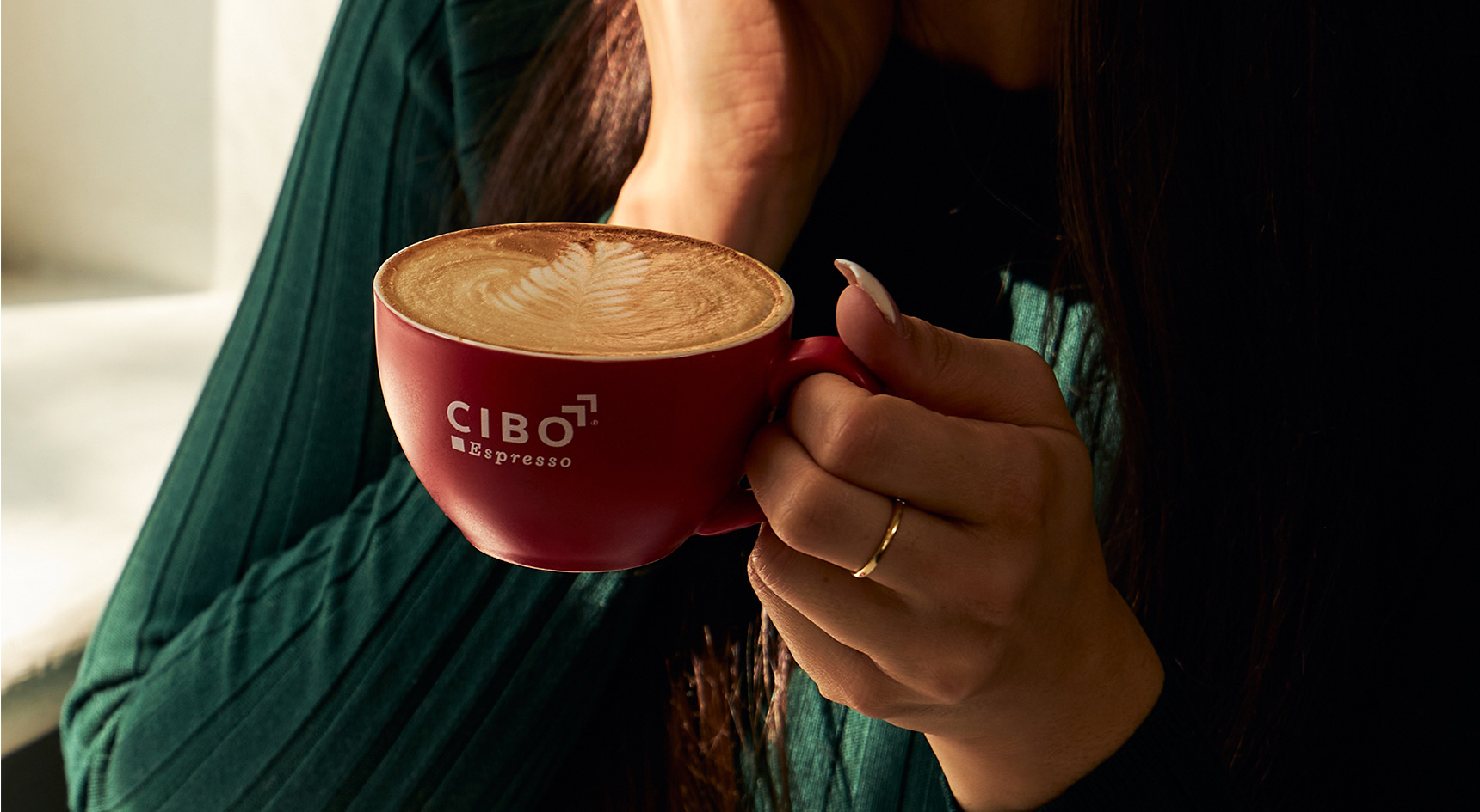 Woman holding cappuccino with CIBO Espresso printed on the mug.