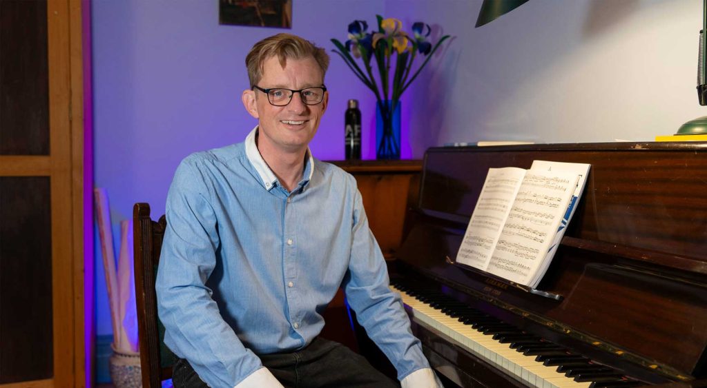 Organ recipient Alex Roose sitting beside his piano.