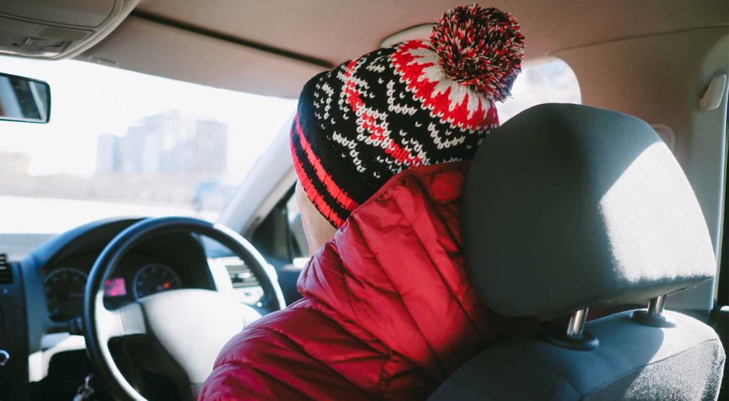 Person wearing a beanie and jacket while sitting at the wheel of a car.