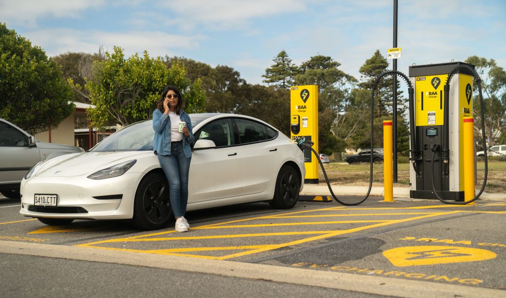 Woman having a cup of coffee while waiting for her electric vehicle to charge at a public charging station.