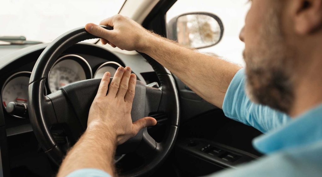 A man honking the car horn in traffic.