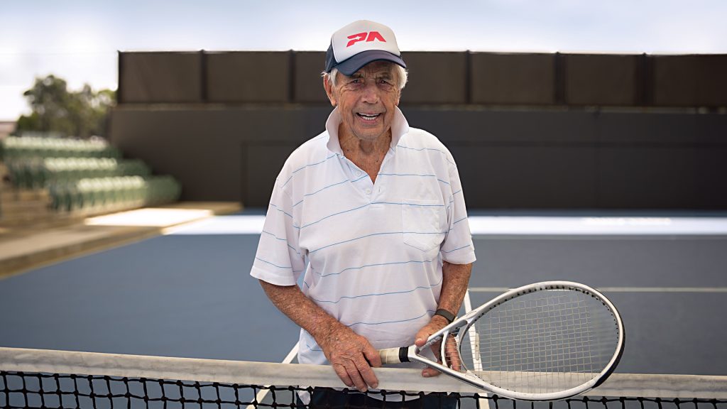 Henry Young standing at a tennis net holding his tennis racquet