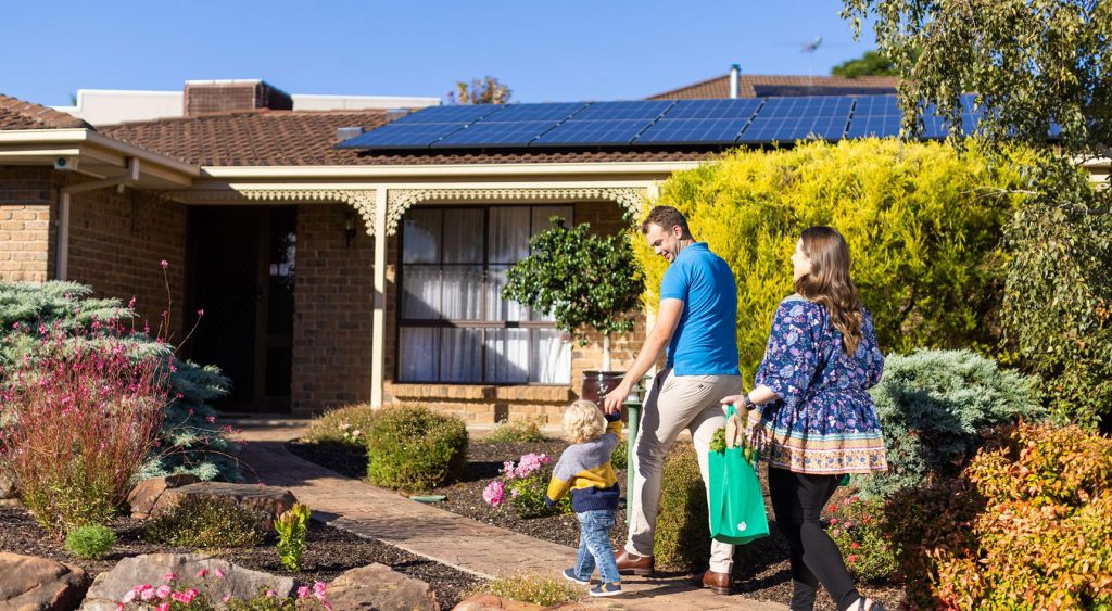 Three-person family coming home to their house that has solar panels