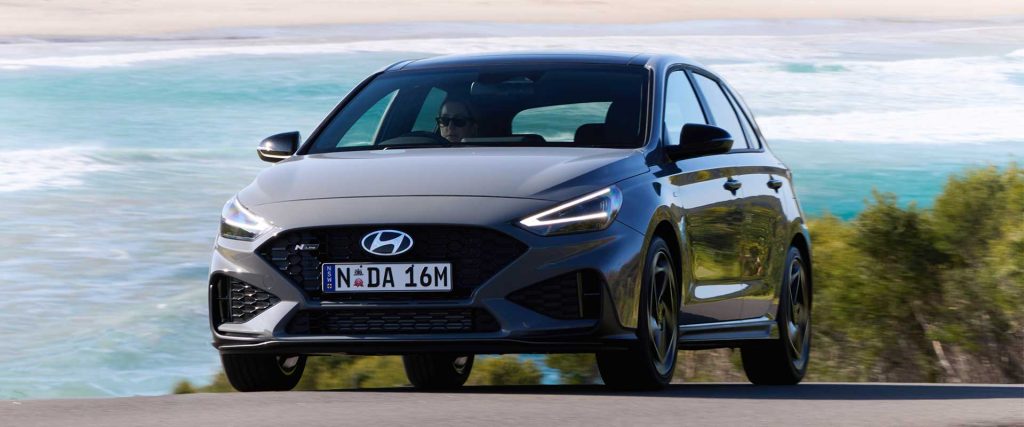 A Hyundai i30N on a road by the beach with its daytime running lights on