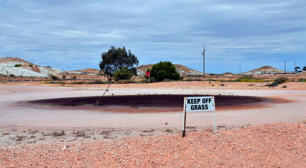 A grassless Coober Pedy Opal Fields Golf Club with a sign reading "Keep off grass:"