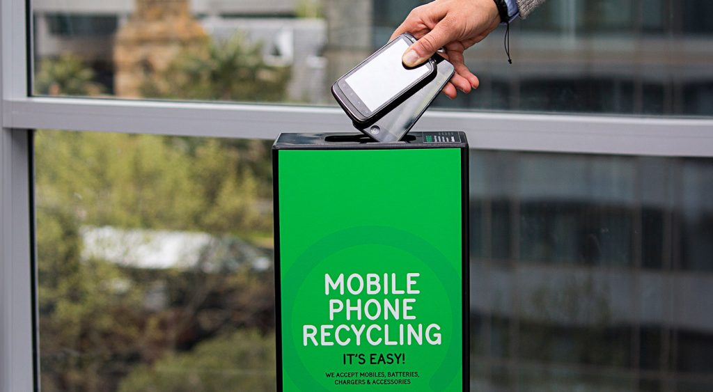 Hand dropping two old phones into a box saying Mobile Phone Recyling, It's easy