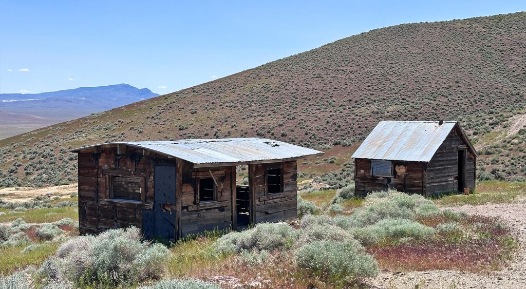 Two dilapidated cabins against a mountainous background.