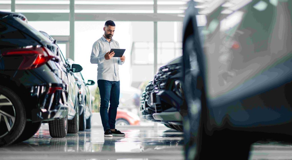 car salesman looking at iPad in showroom.